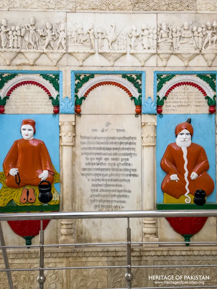Close view of painted relief portraits of two seated saints flanking an inscribed marble panel at Sadhu Belo Temple