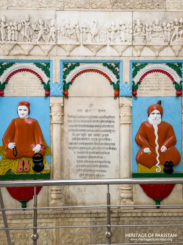 Close view of painted relief portraits of two seated saints flanking an inscribed marble panel at Sadhu Belo Temple