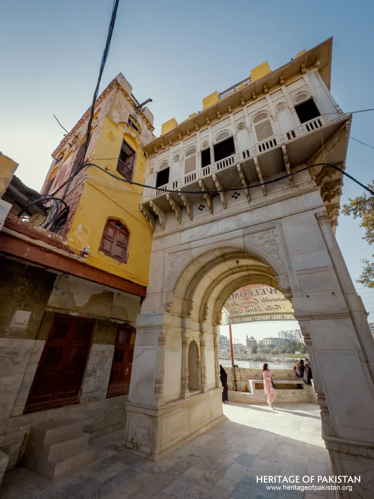 Marble archway gateway to Sadhu Belo Temple beside a weathered yellow building