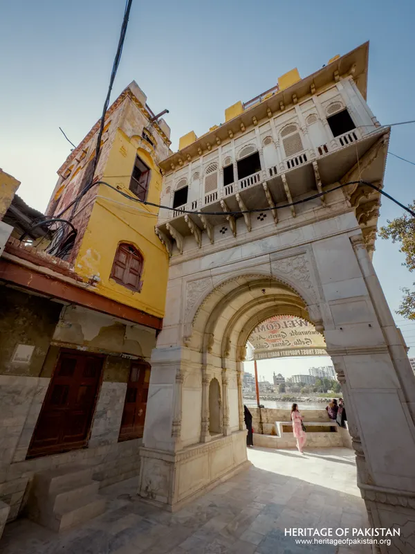 Marble archway gateway to Sadhu Belo Temple beside a weathered yellow building