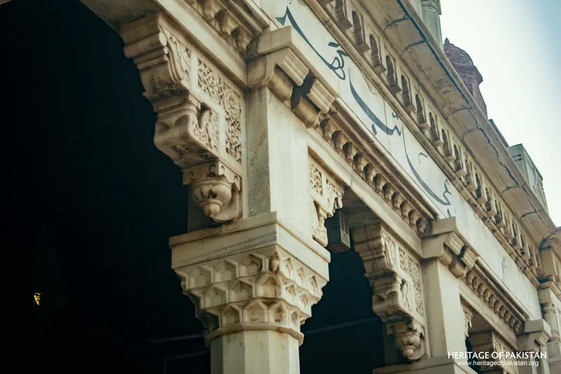 Carved stone column capitals and arch soffit with Urdu script above