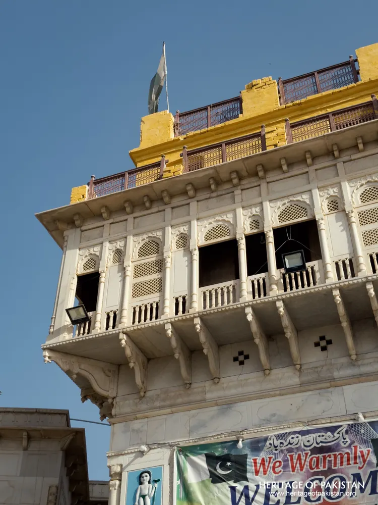 Angled view of the marble tower's carved balcony and golden crown at Sadhu Belo Temple