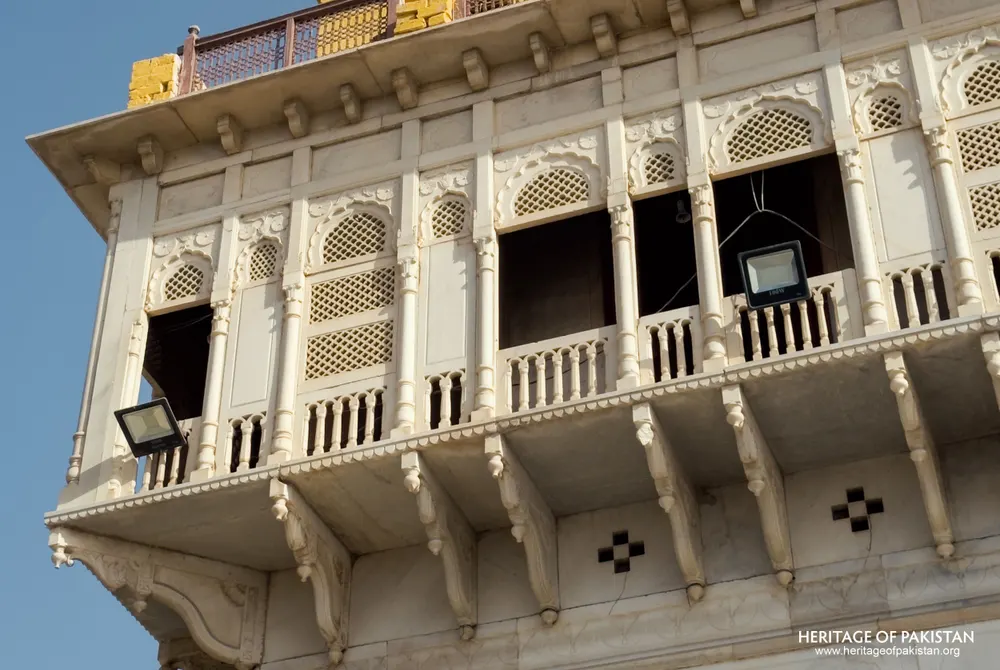 Wide angle of the carved marble balcony tier crowned by a golden lattice terrace at Sadhu Belo Temple
