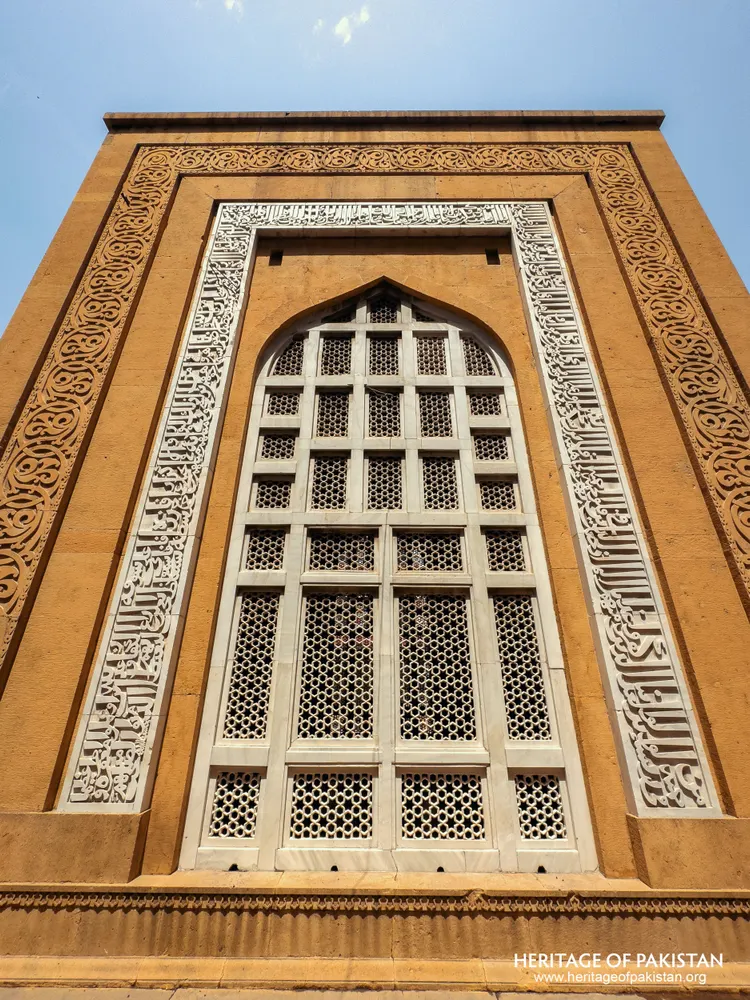 Arched white jali screen set in a yellow sandstone wall with carved border
