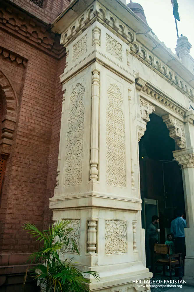 White marble pillar with carved panels beside a red-brick wall