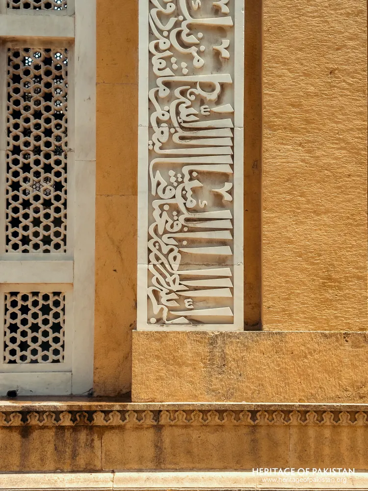White marble calligraphy panel set into a yellow stone wall, with a pierced lattice screen to the left