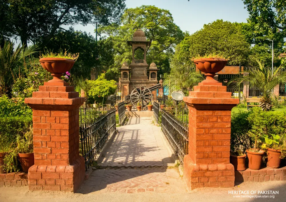 Red brick gate pillars with stone urns flanking an iron-railed path