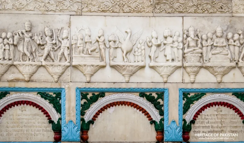 Carved marble frieze of narrative relief scenes above coloured scalloped arches at Sadhu Belo Temple
