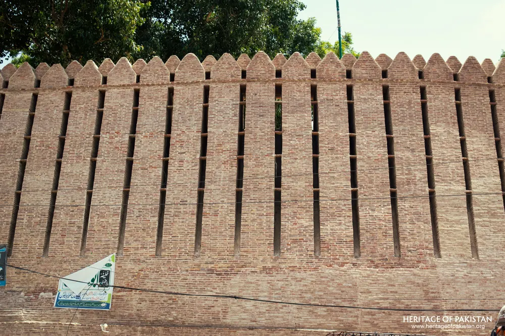 Frontal view of Pakka Qila's crenellated rampart with a small signboard at its base
