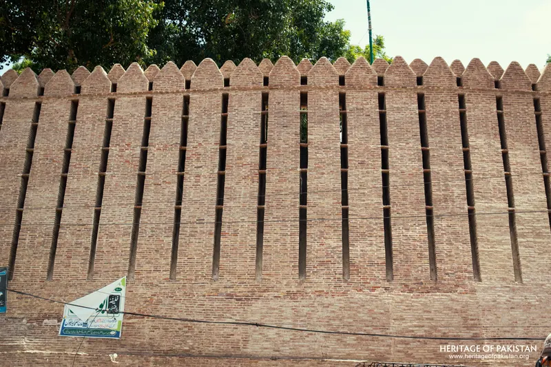 Frontal view of Pakka Qila's crenellated rampart with a small signboard at its base