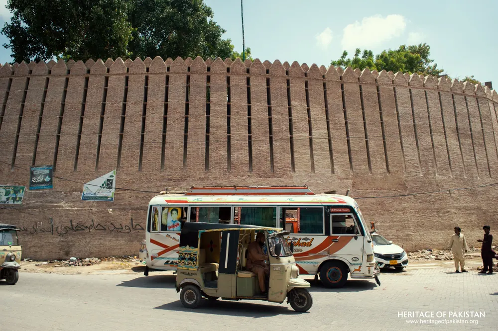 Crenellated rampart of Pakka Qila above a street with a parked bus and rickshaw