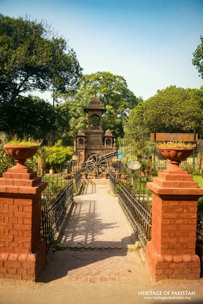 Iron-railed pathway between red brick pillars leading to a cannon on a wheeled carriage