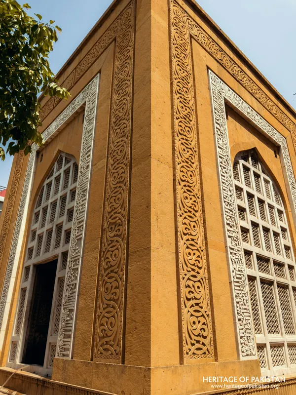 Corner of a yellow stone structure with white carved scroll borders and arched jali screens