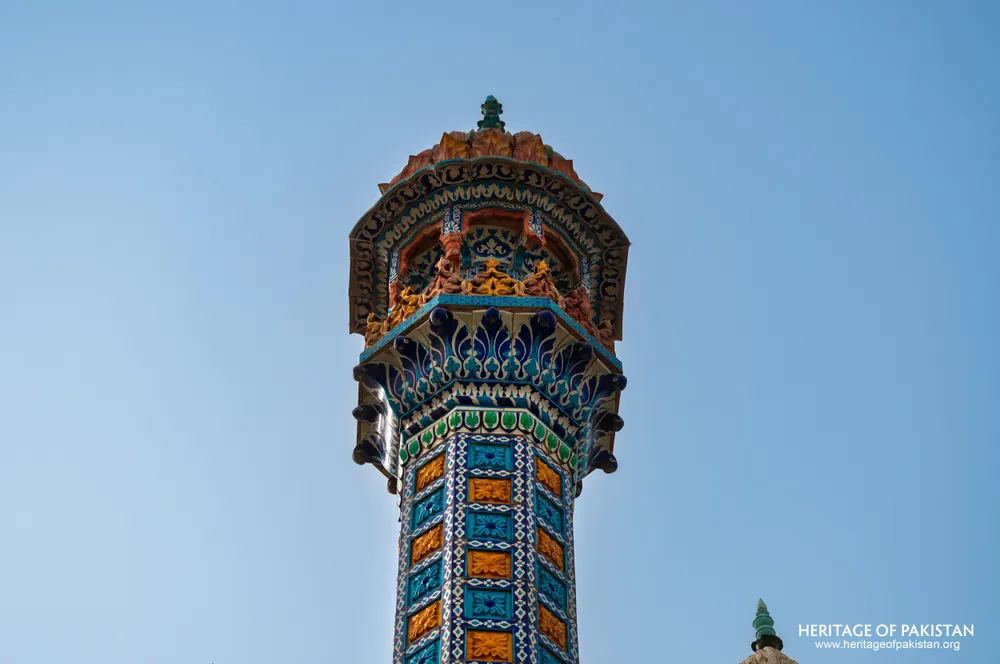 Top of a tiled minaret with a corbelled balcony against the sky