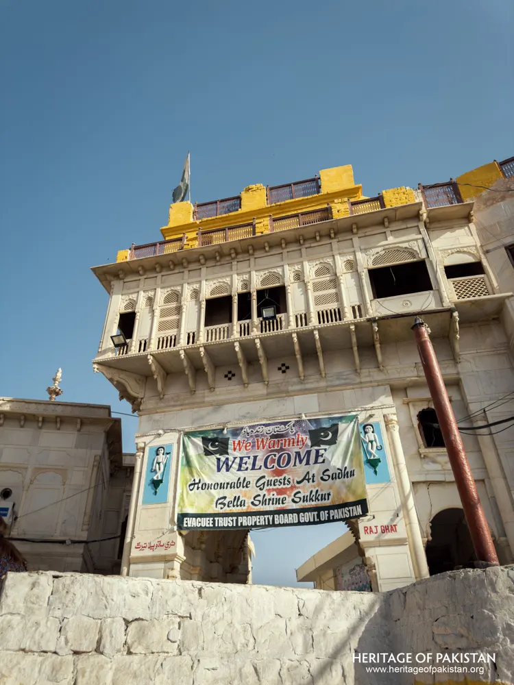 Sadhu Belo Temple's tower rising above the whitewashed stone entrance with a welcome banner