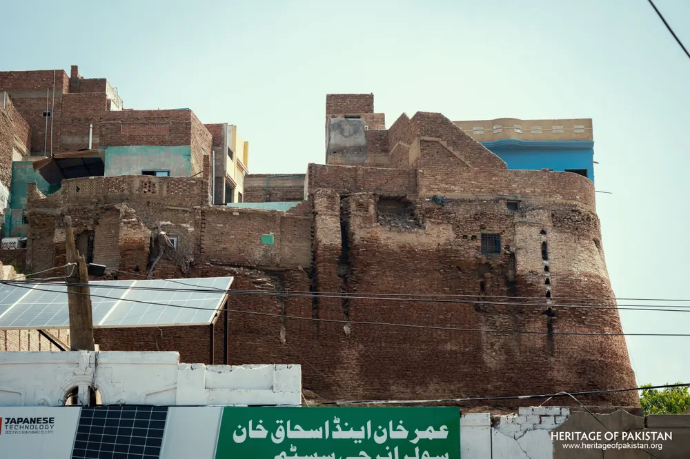 Weathered upper brickwork of Pakka Qila rising above modern rooftop additions