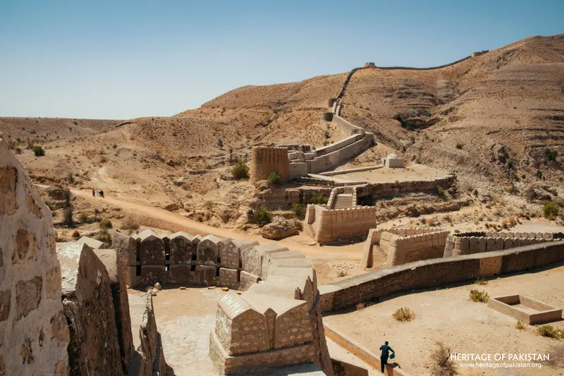 Crenellated stone walls descending a dry hillside with a figure below