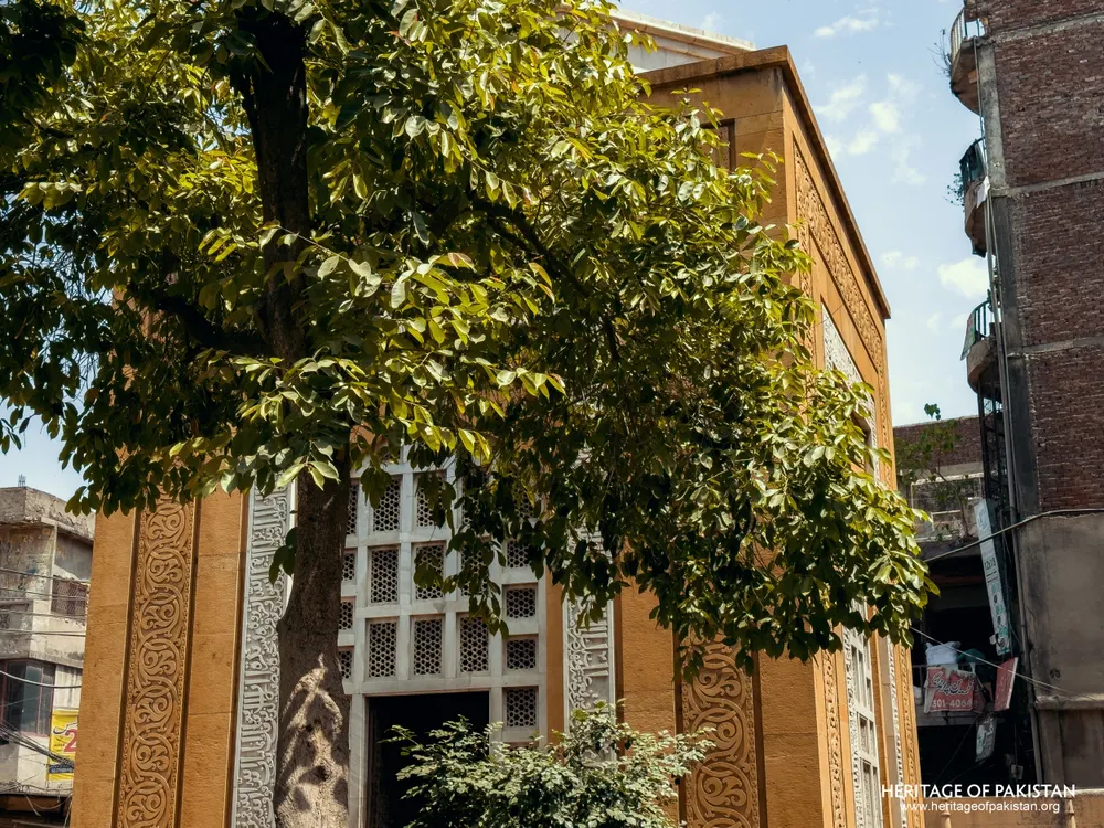 Yellow sandstone wall with white jali screen, partly obscured by a tree