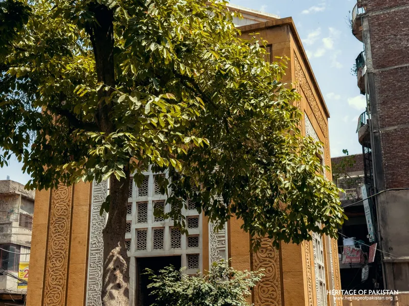 Yellow sandstone wall with white jali screen, partly obscured by a tree