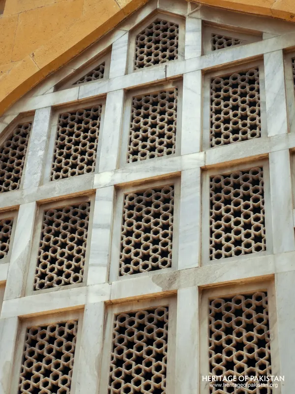 Arched window filled with a grid of pierced stone lattice panels in white marble framing