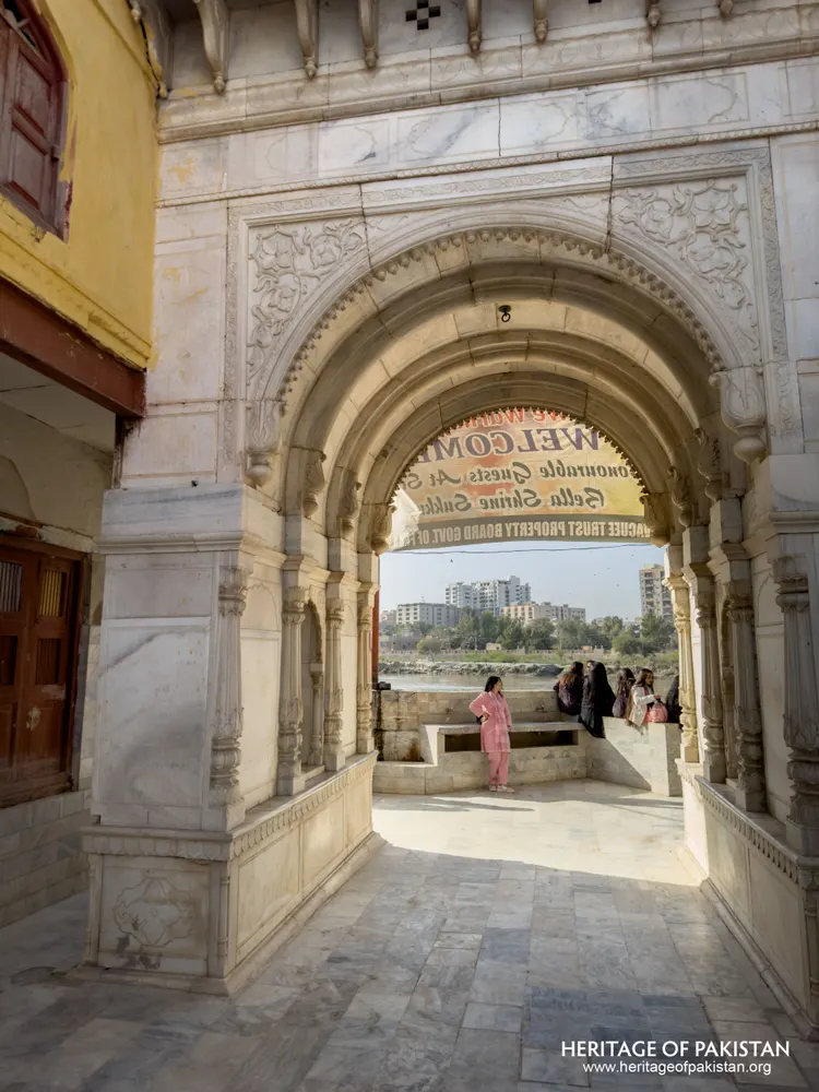 Carved marble archway framing a river view with visitors at Sadhu Belo Temple