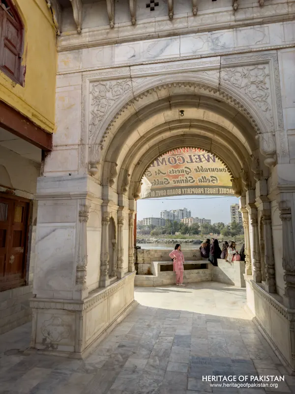 Carved marble archway framing a river view with visitors at Sadhu Belo Temple