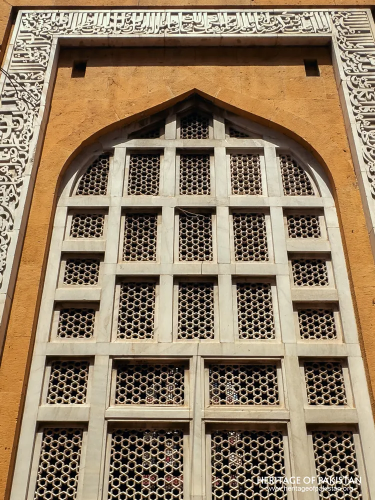 Close-up of a pointed-arch white jali screen in a yellow sandstone wall