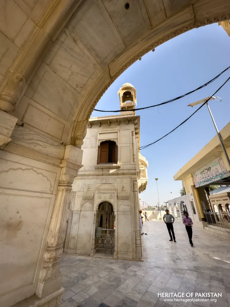 View through the marble archway toward the domed bell tower and courtyard walkway at Sadhu Belo Temple
