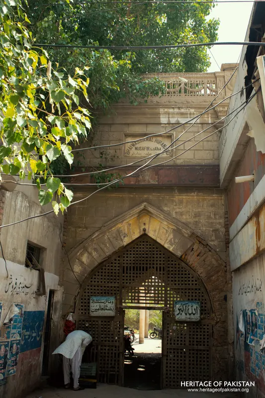 Arched wooden gateway of the Musafirkhana at Pakka Qila with a man bending at the threshold