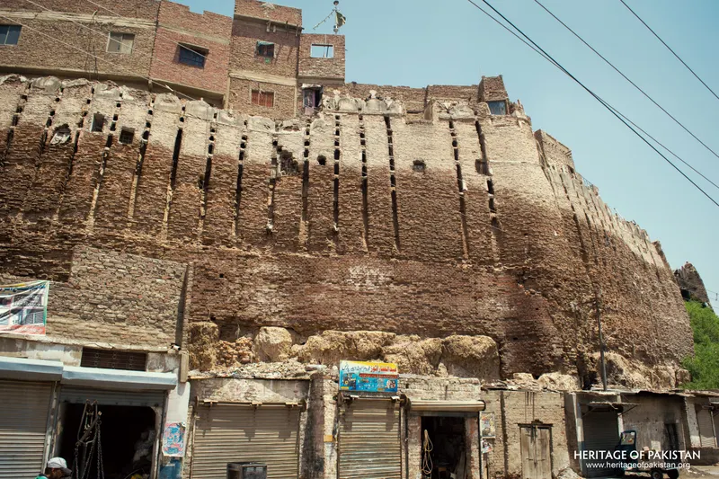 Wide view of Pakka Qila's rampart above a market street with shuttered shops and a parked rickshaw