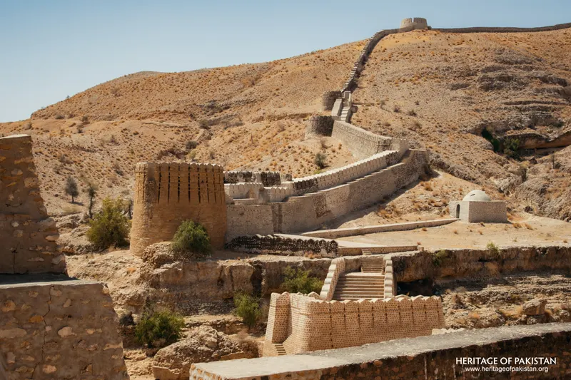 Brick tower and wall climbing a hillside, small domed structure below