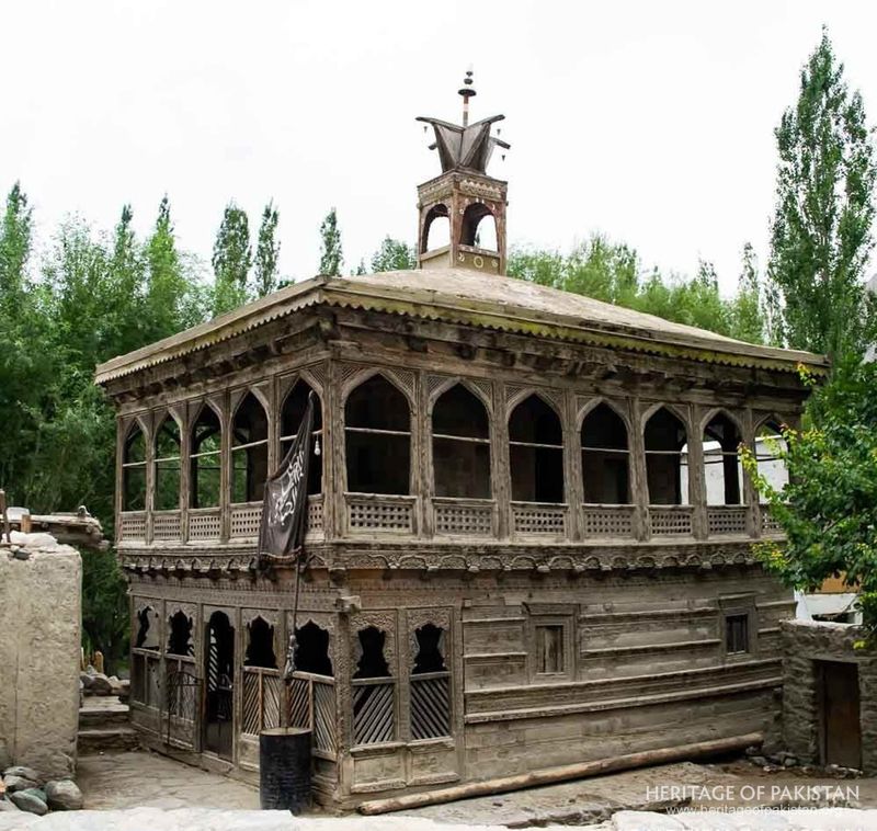 Ornate wooden mosque stands amid tall poplar trees in daylight.