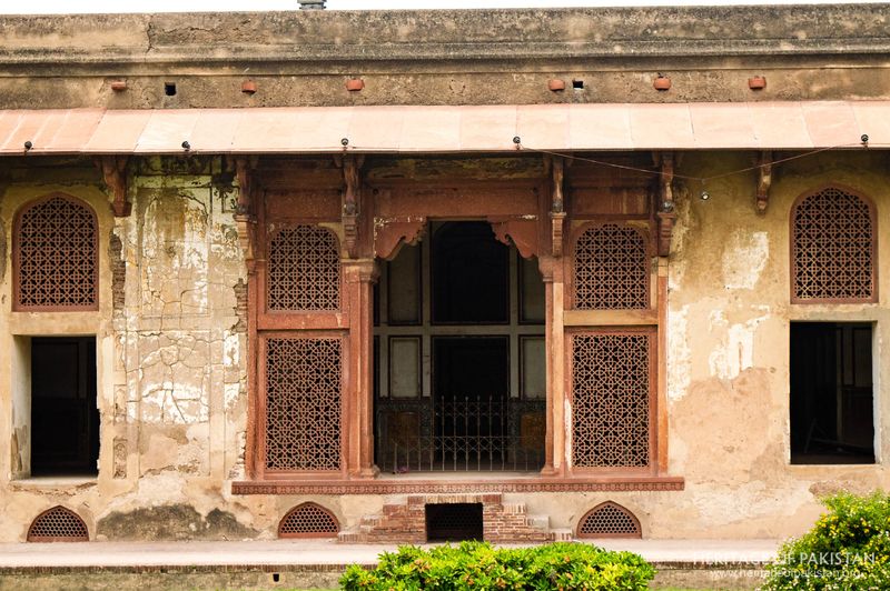 Ornamental latticed screens set within arched recesses in deteriorating wall.